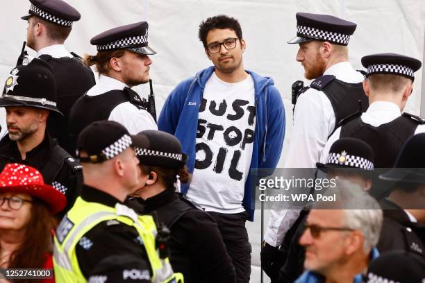 Police officers detain a member of "Just Stop Oil" movement as people gather to watch the procession during the Coronation of King Charles III and...