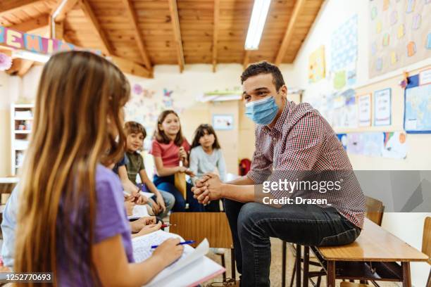insegnante con maschera facciale che motiva i bambini ad essere attivi in classe dopo il coronavirus - spiegare foto e immagini stock