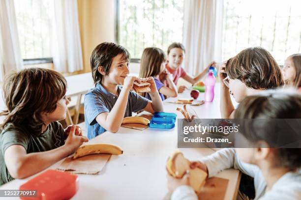 kinder essen in der schule und halten sozialen abstand - kantine essen stock-fotos und bilder