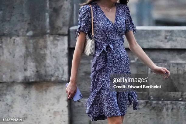 Passerby wears a gray and white checked Vuitton small bag, a navy blue ruffled floral print v-neck dress, a necklace, on June 25, 2020 in Paris,...