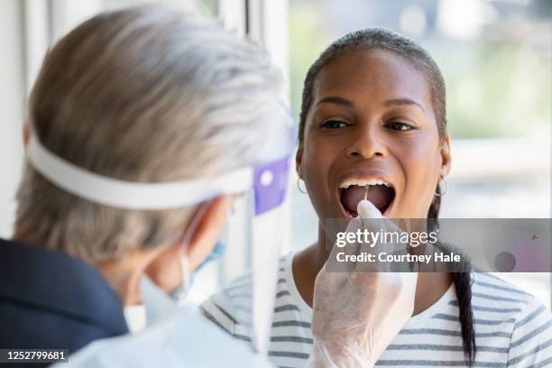woman opens mouth for cheek and throat swab while being tested for covid-19 coronavirus - cheek stock pictures, royalty-free photos & images
