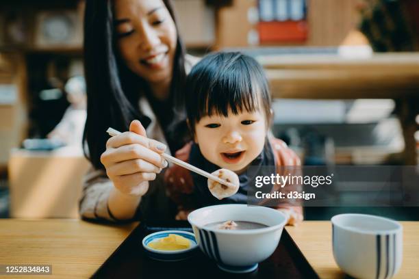 joyful young asian mother and cute little daughter sharing a japanese style dessert red bean soup with mochi in a traditional style kissaten cafe restaurant - mochi stock-fotos und bilder