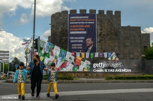 Pedestrians walk past a banner with a portrait of Turkish President Recep Tayyip Erdogan hanging on historical Sur castle behind election campain...