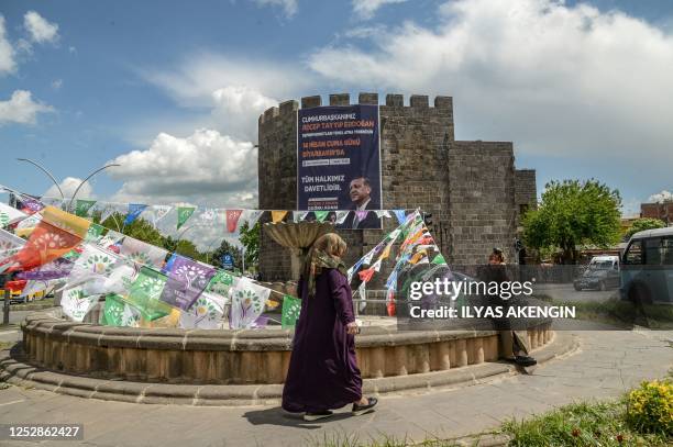 Woman walks past election campain flags of People's Democratic Party and a banner with a portrait of Turkish President Recep Tayyip Erdogan hanging...