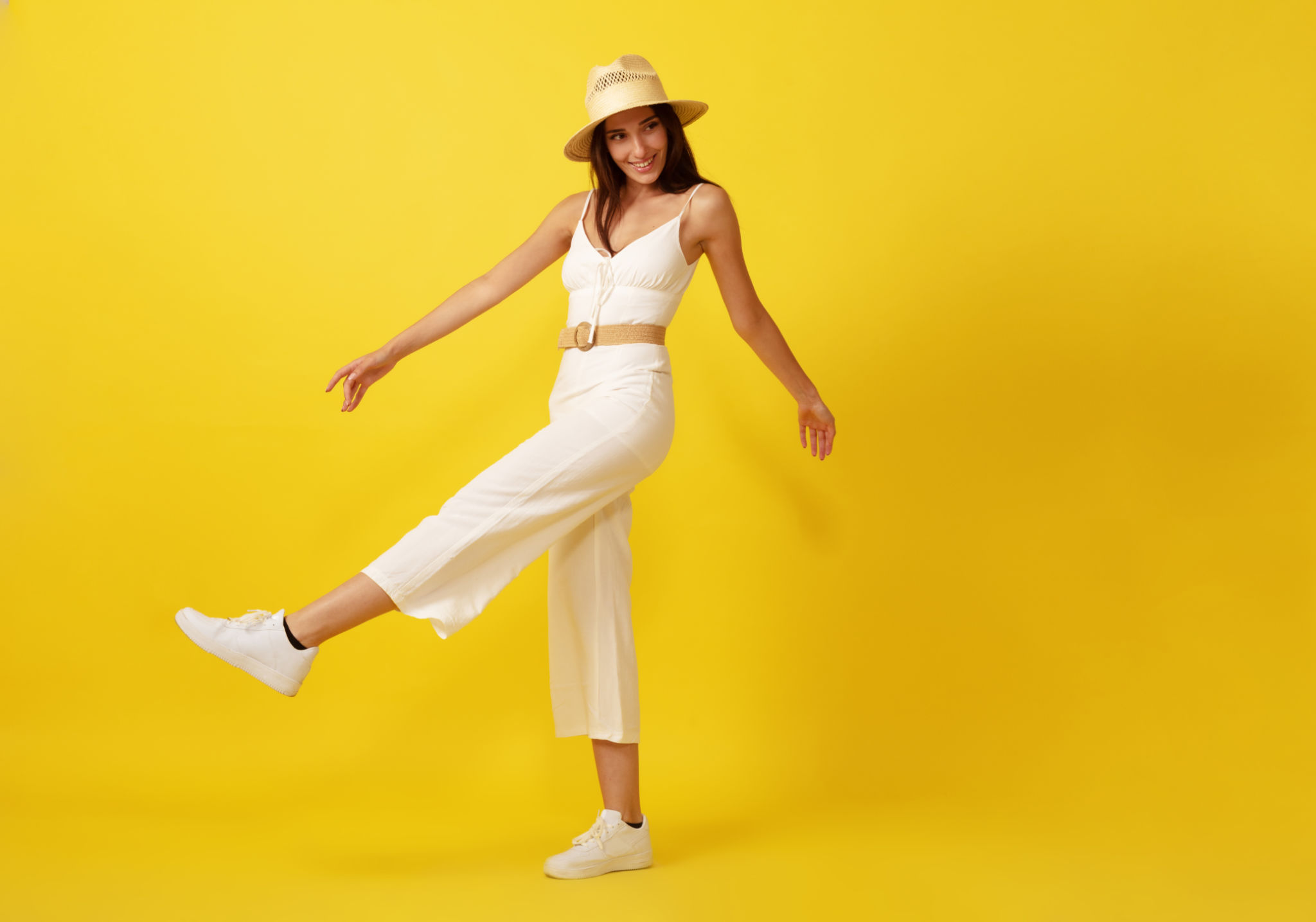 Beautiful young woman walking with straw hat in white dress front of yellow background. Beautiful young woman walking with straw hat in white dress front of yellow background.