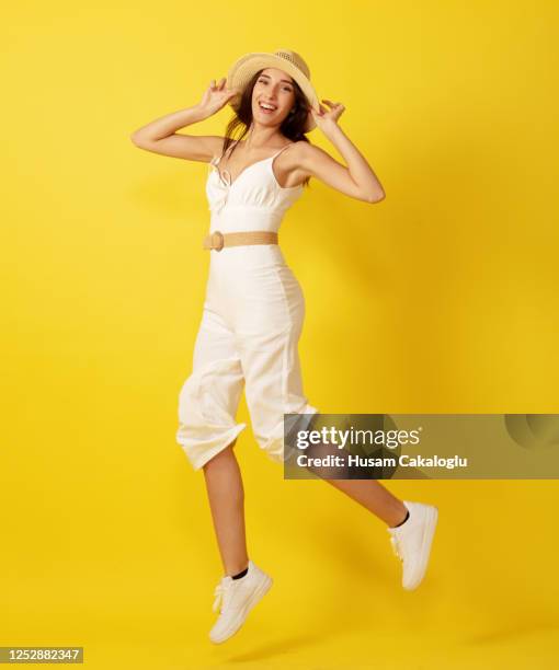 beautiful young woman jumping with straw hat in white dress front of yellow background. - woman full body isolated stock pictures, royalty-free photos & images