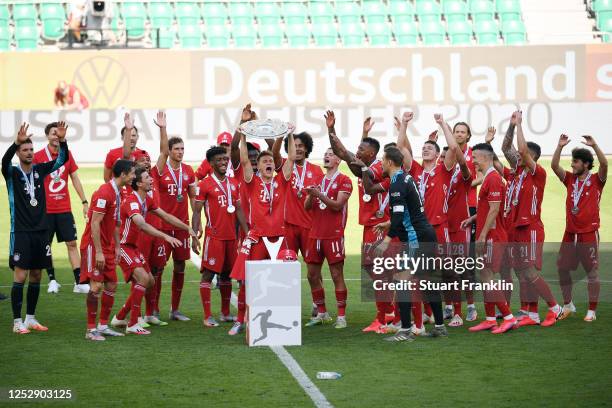 Joshua Kimmich of FC Bayern Muenchen lifts the trophy to celebrate the championship following the Bundesliga match between VfL Wolfsburg and FC...