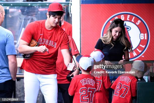 Shohei Ohtani of the Los Angeles Angels gives his autograph to kids in the dugout before the game against the Texas Rangers at Angel Stadium of...