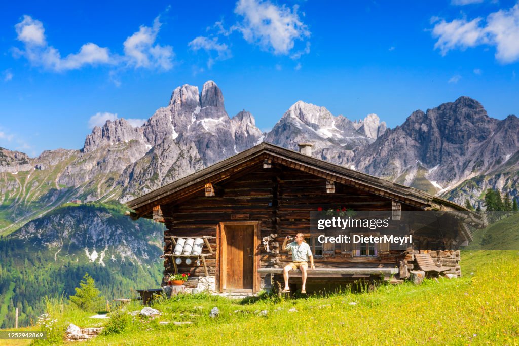 Mens gekleed in traditionele Oostenrijkse of Beierse klerenzitting op bank voor alpiene hut, die van bier in Alpen geniet