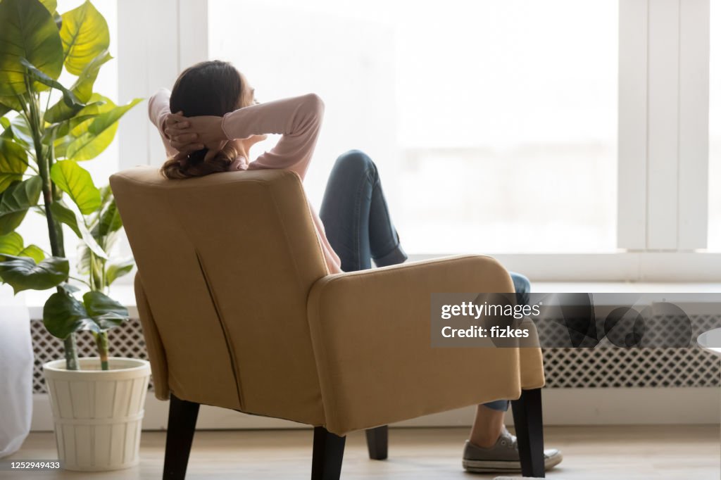年輕女子在舒適的扶手椅后視圖休息。