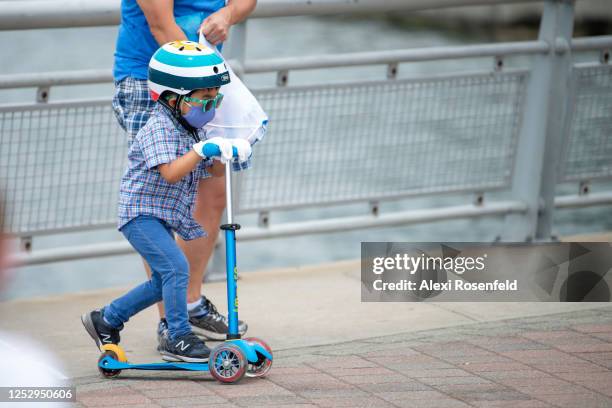 Child wearing a mask and gloves rides a scooter as the city moves into Phase 2 of re-opening following restrictions imposed to curb the coronavirus...
