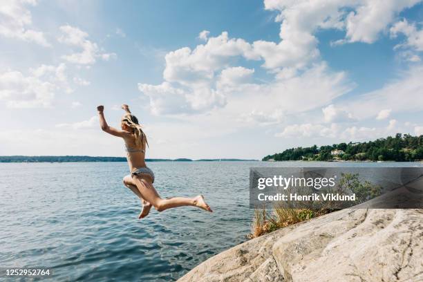 kid jumping from cliff into water in summer - stockholm summer stock-fotos und bilder