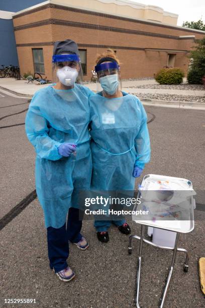 zwei krankenschwestern lächeln, während sie kleider, chirurgische gesichtsmasken, handschuhe und gesichtsschilde tragen, während sie auf patienten in einem drive-up (drive-through) covid-19 (coronavirus) warten, während sie im freien auf patienten wart - schutz und arbeitskleidung stock-fotos und bilder