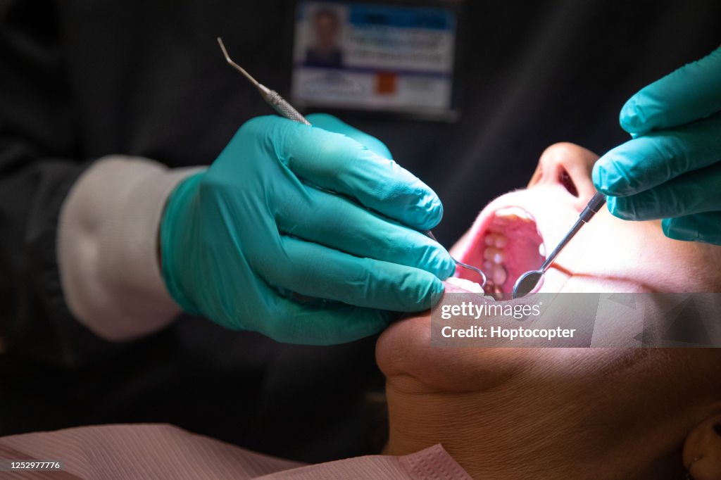 Ein Zahnarzt, der chirurgische Handschuhe trägt, verwendet ein Lupenlicht, um die Zähne einer weiblichen Patientin in ihren sechziger Jahren in einer Zahnklinik zu untersuchen