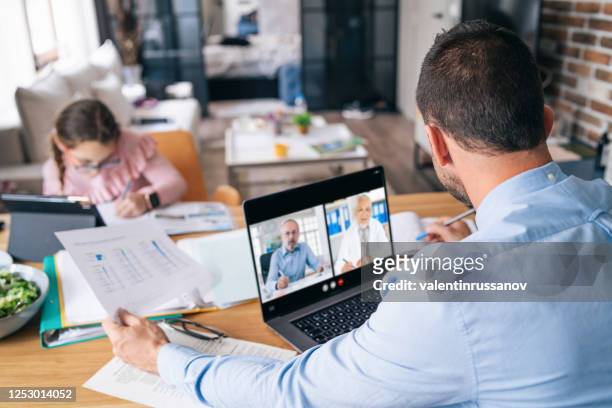 father trying to talk with doctor on laptop while staying at home. homeschooling and distance learning, during covid-19 - remote location stock pictures, royalty-free photos & images
