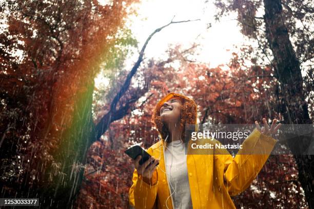 happy young woman in raincoat on a rainy day listening music looking at rainbow - chuva imagens e fotografias de stock