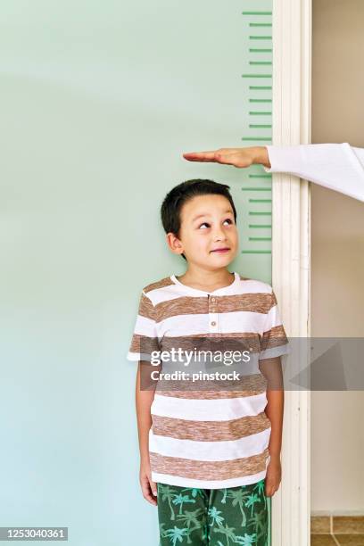 madre midiendo la altura de su hijo en la pared. está creciendo tan rápido. - height fotografías e imágenes de stock