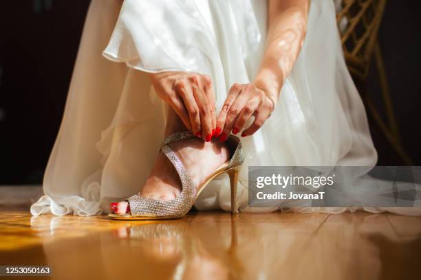 bride putting on her shiny wedding high heels - wedding feet stock-fotos und bilder