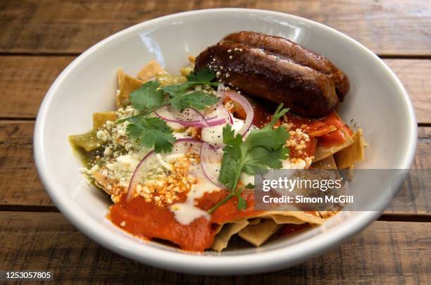 chilaquiles with salsa verde and salsa rojo and sausage in a white bowl on a wooden table - chilaquiles fotografías e imágenes de stock