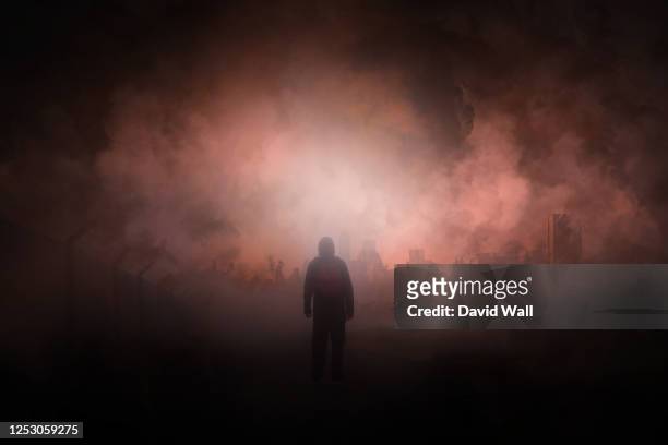 a post apocalypse scene showing a man standing in a ruined city looking at a destroyed city. with smoke covering the sky. - armageddon stock-fotos und bilder