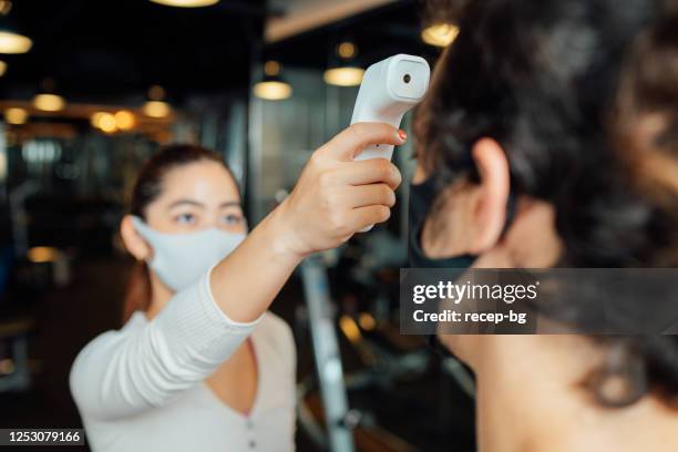 female gym owner using infrared thermometer to check customer's body temperature - ladies first screening reception stock pictures, royalty-free photos & images