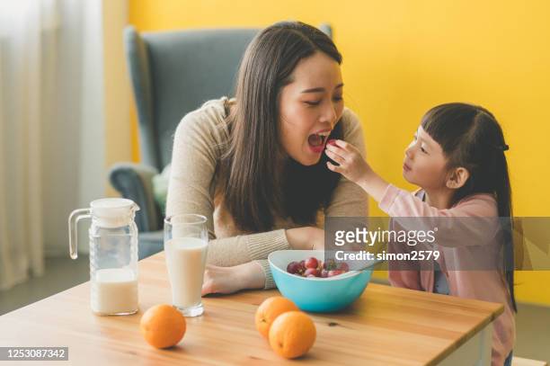 leuke dochter die haar moederdruif in woonkamer voedt - moeder kind zes melk stockfoto's en -beelden
