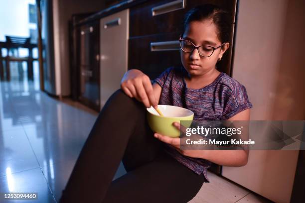 girl eating from bowl while sitting on kitchen floor - trastorno de alimentación fotografías e imágenes de stock