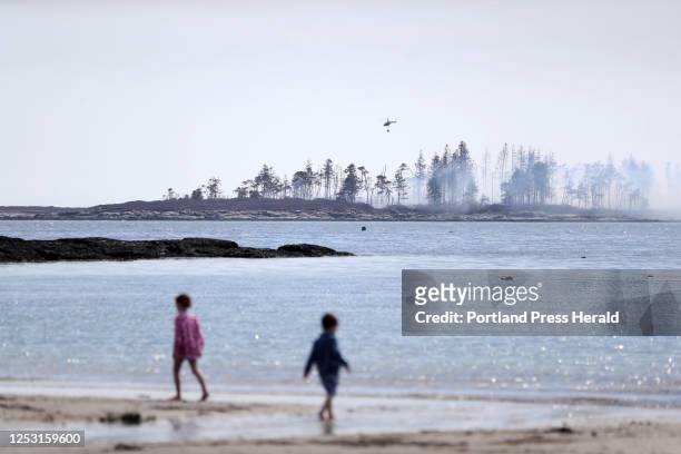 Children walk on the beach at Kettle Cove State Park as a helicopter prepares to douse fire from a controlled burn on Richmond Island on Friday...