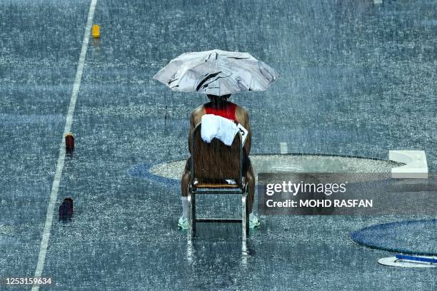 Thailand's Patsapong Amsam-ang waits under an umbrella during a break due to heavy rains in the men's pole vault final during the 32nd Southeast...