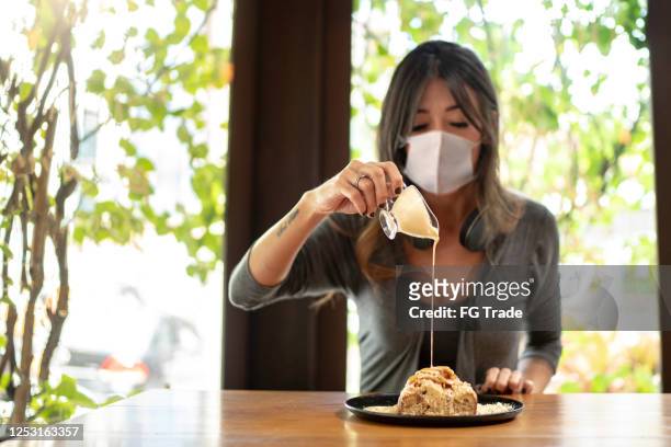 donna che versa condimento cremoso in un pane dolce usando maschera protettiva - condensed milk foto e immagini stock