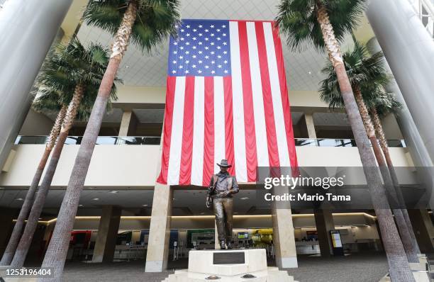 Statue of John Wayne is on display beneath an American flag in John Wayne Airport, located in Orange County, on June 28, 2020 in Santa Ana,...