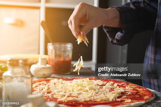 cooking italian vegetarian pizza with vegetables and mushrooms at home, on a wooden table. the woman puts and sprinkles grated cheese on the dough. step-by-step instructions, do it yourself. step 4. - sprinkling imagens e fotografias de stock