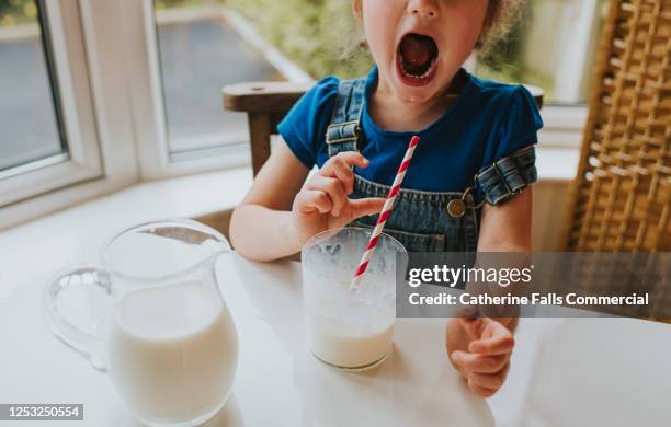 surprised little girl drinking a glass of milk with a paper straw - almond milk stock-fotos und bilder