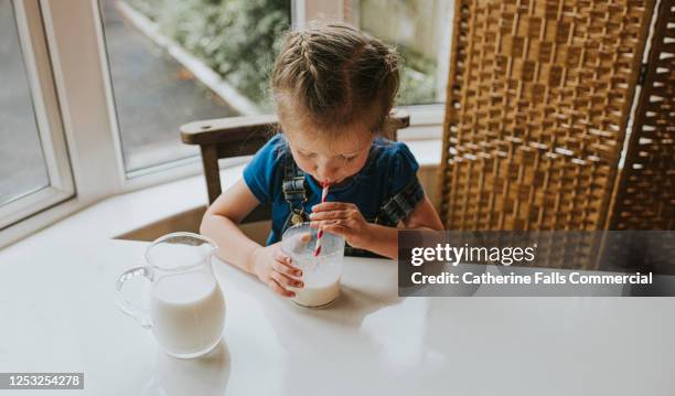 surprised little girl drinking a glass of milk with a paper straw - sucking fotografías e imágenes de stock