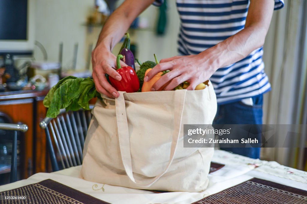 Hombre asiático desempaquetando comestibles en la isla de la cocina