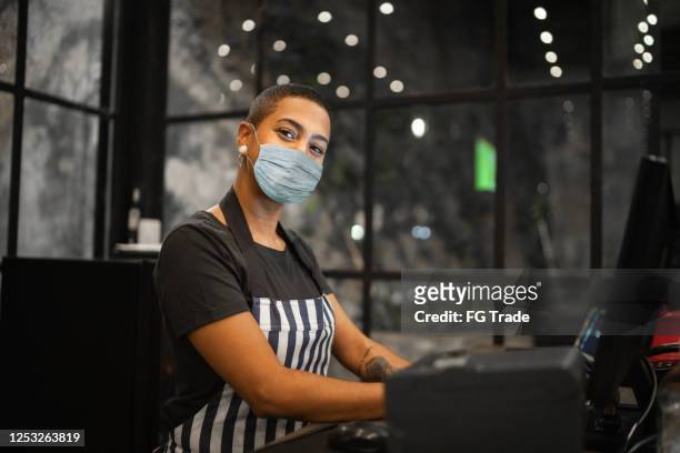 portrait of a waitress typing on cash register using protective mask - restaurant mask stock pictures, royalty-free photos & images
