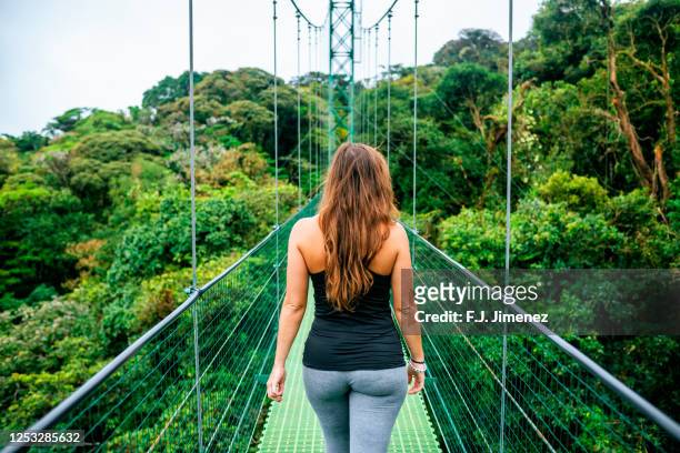 woman walking on suspension bridge in monteverde, costa rica - monteverde costa rica stock pictures, royalty-free photos & images