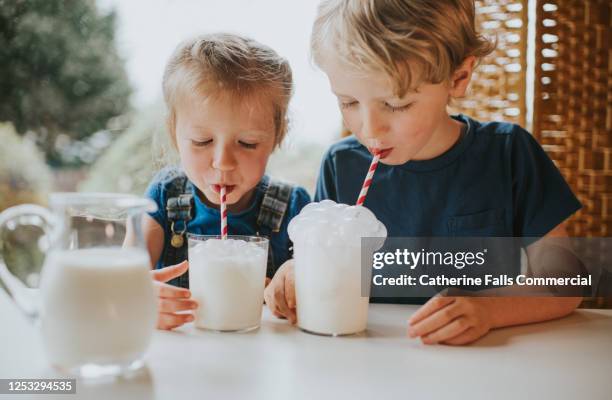 kids blowing bubbles into a glass of milk with a paper straw - milchwaren stock-fotos und bilder