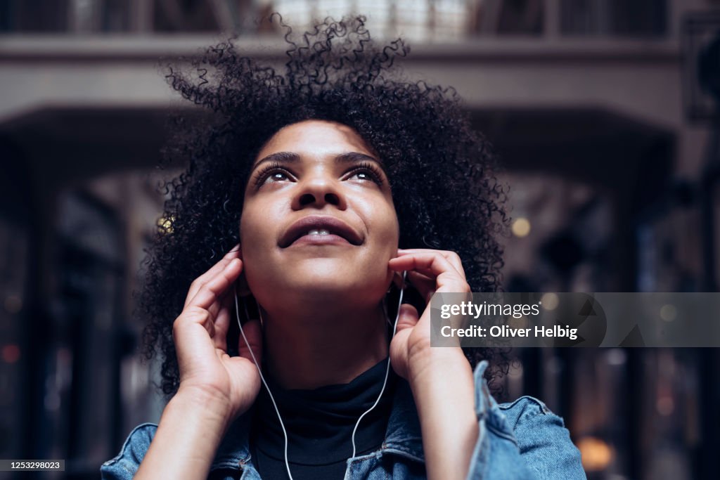 An attractive young woman with African American roots listens to music with headphones. She looks up dreamily and smiles slightly