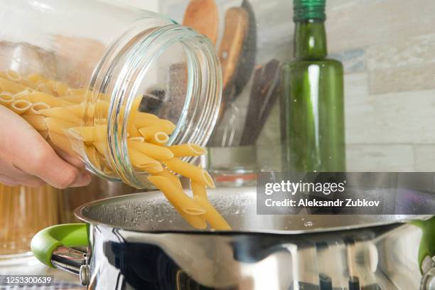 cooking italian pasta with cream sauce and basil, at home. a girl or woman adds and throws raw penne macaroni into boiling water from a glass jar. vegetarian food. step-by-step instructions, do it yourself. step 3. - boiling pasta stock pictures, royalty-free photos & images