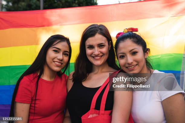 trois jeunes femmes adultes contre un drapeau arc-en-ciel de fierté - polyamour photos et images de collection