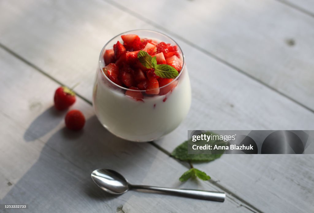 Summer dessert with red strawberry berries, mint and natural yougurt. Idea for breakfast. White wooden table rustic background.