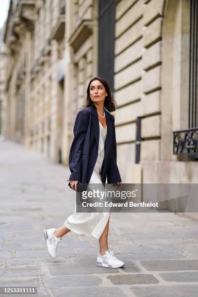 Geraldine Boublil wears a white pearl necklace from Coconut Love, a dark navy blue striped oversized blazer jacket from Gauge 81, a white lustrous...