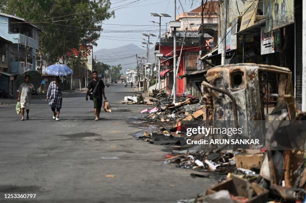 People walk past a burnt vehicle and rubble on a street in Churachandpur in violence hit areas of northeastern Indian state of Manipur on May 9,...