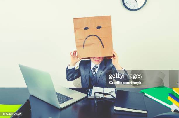 a young boy dressed as a businessman wears a paper bag with a sad face on it. - evasion fiscale stock pictures, royalty-free photos & images