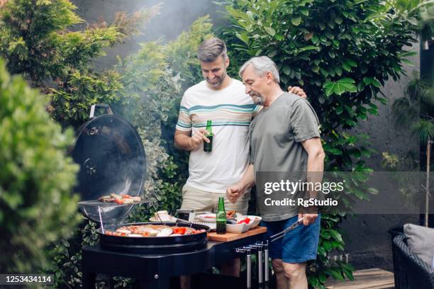mid adult man preparing barbecue with his dad - senior men beer stock pictures, royalty-free photos & images