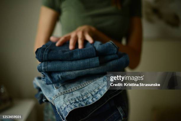 young woman, wearing green t-shirt,  holding a pile of folded jeans in her both hands - green pants ストックフォトと画像