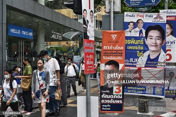 People walk past various political party's campaign banners along a street in Bangkok on May 10 ahead of the May 14 Thailand general election.