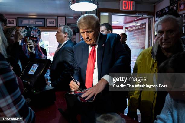 Manchester, NH Former President Donald Trump signs a backpack for Micki Larson-Olson while visiting the Red Arrow Diner after a campaign rally on...