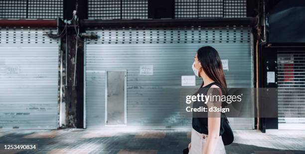 young asian woman looking at closed shops while walking on city street. economic depression due to covid-19 outbreak - city of detroit teeters on bankruptcy as state audits its finances stockfoto's en -beelden